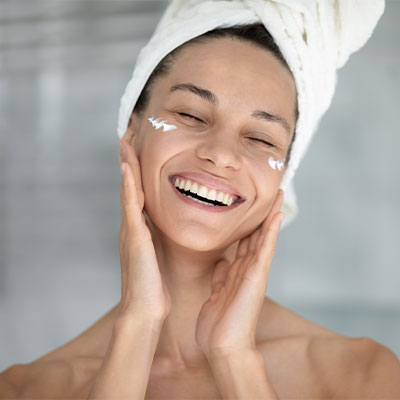 An excited woman happily applying Pevonia products during her get-ready routine.