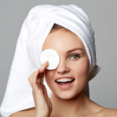 Teenage girl with a towel wrapped around her hair, covering one eye with a circular cotton pad.
