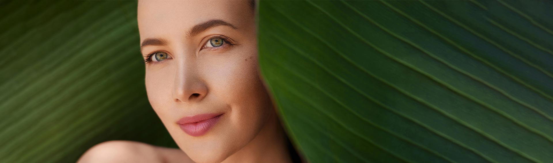 A woman's face in between large, tropical leaves.