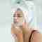 A woman cleansing her face with a towel on her head.
